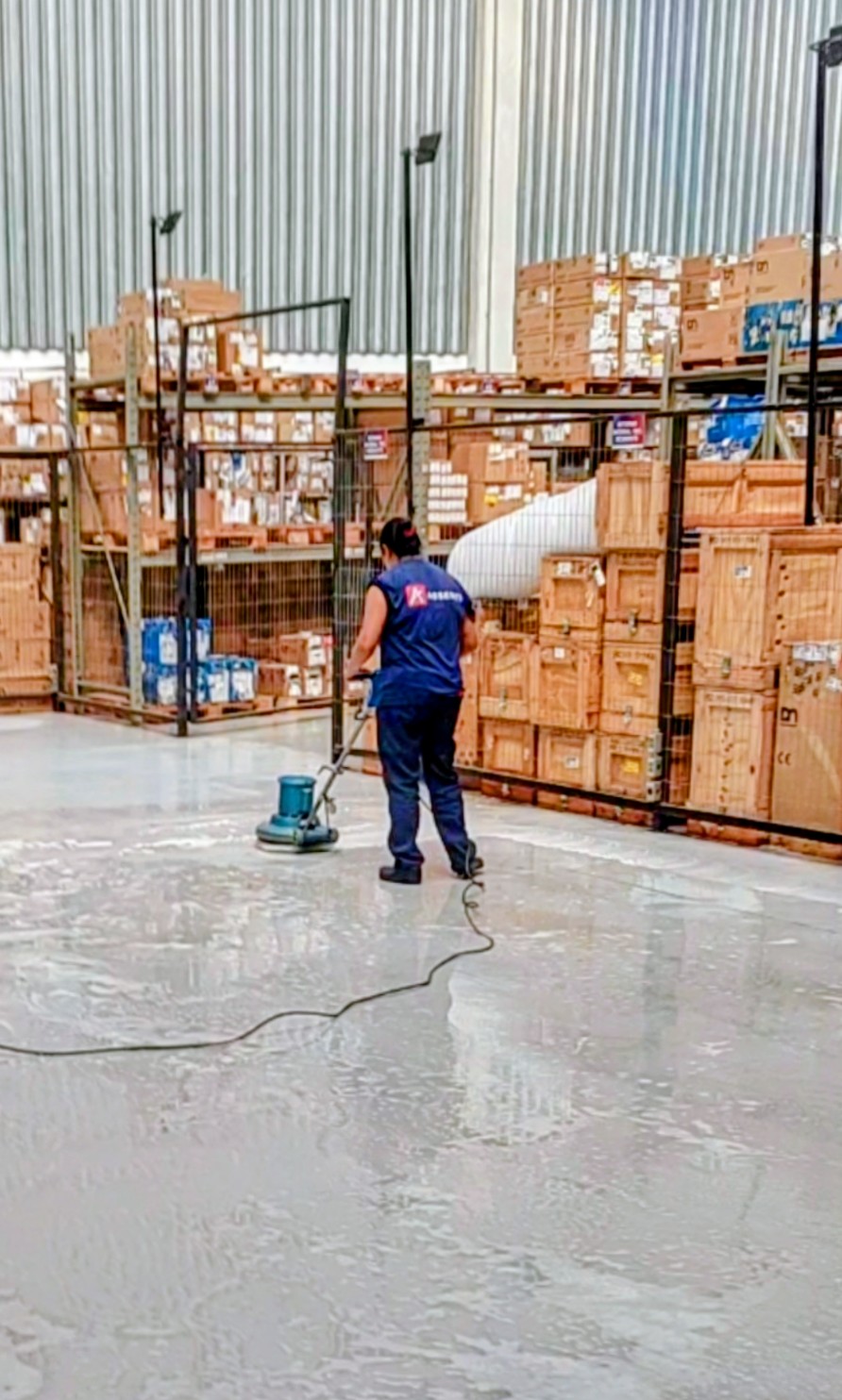 Profissional realizando a limpeza do piso de um galpão com uma enceradeira industrial